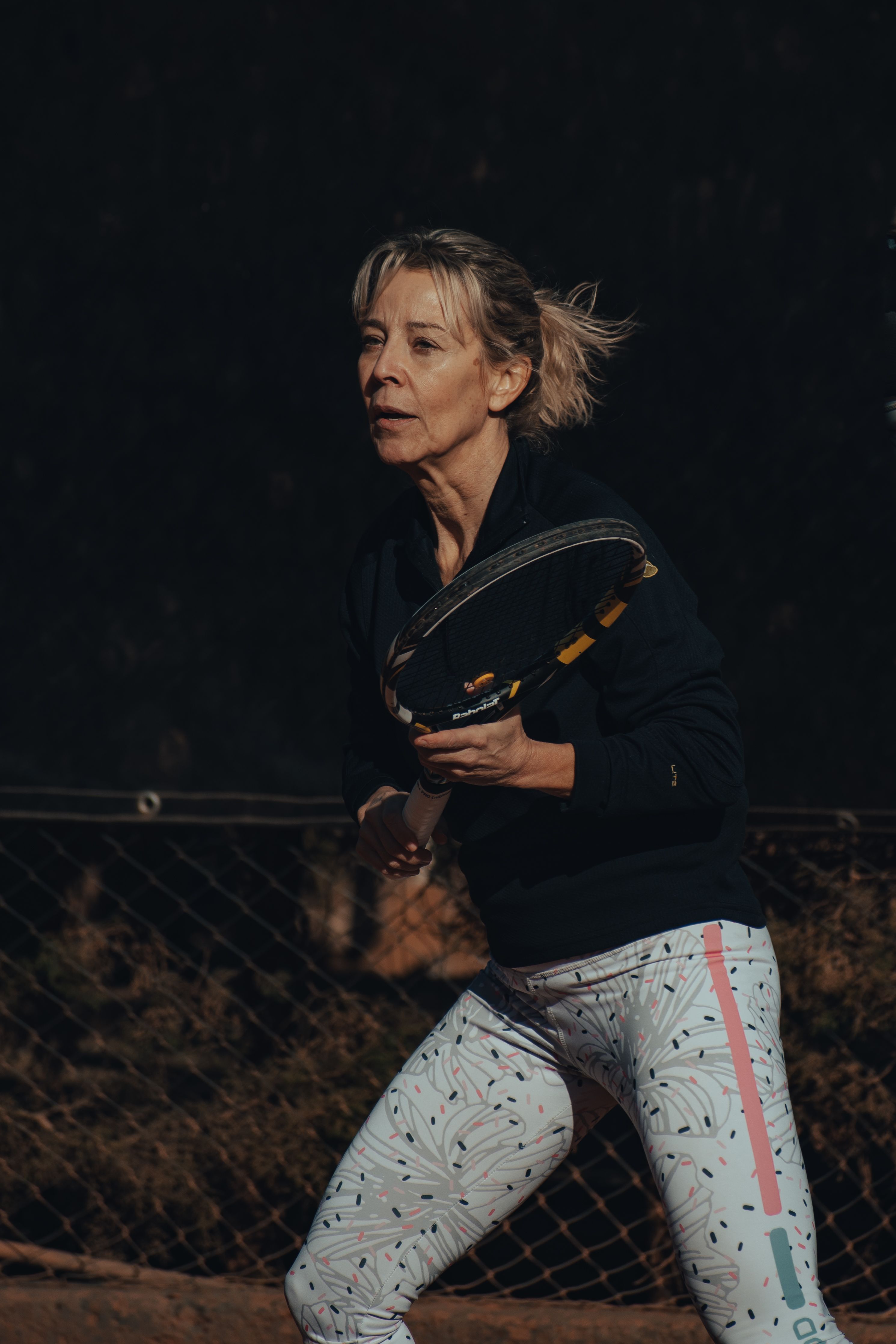 A mature adult tennis player preparing to return a ball on an outdoor court