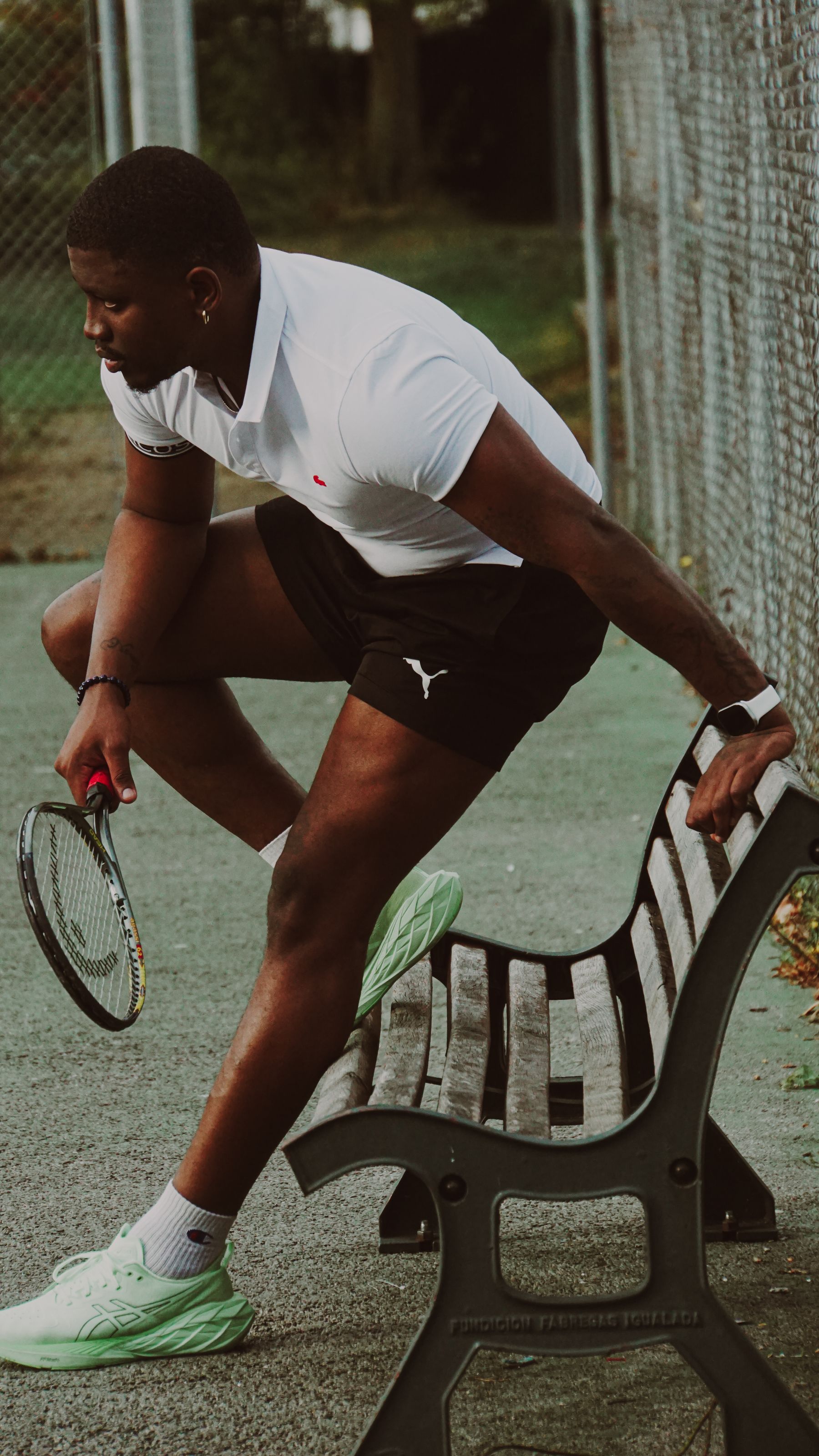An adult tennis player holding a racket while seated on a courtside bench.