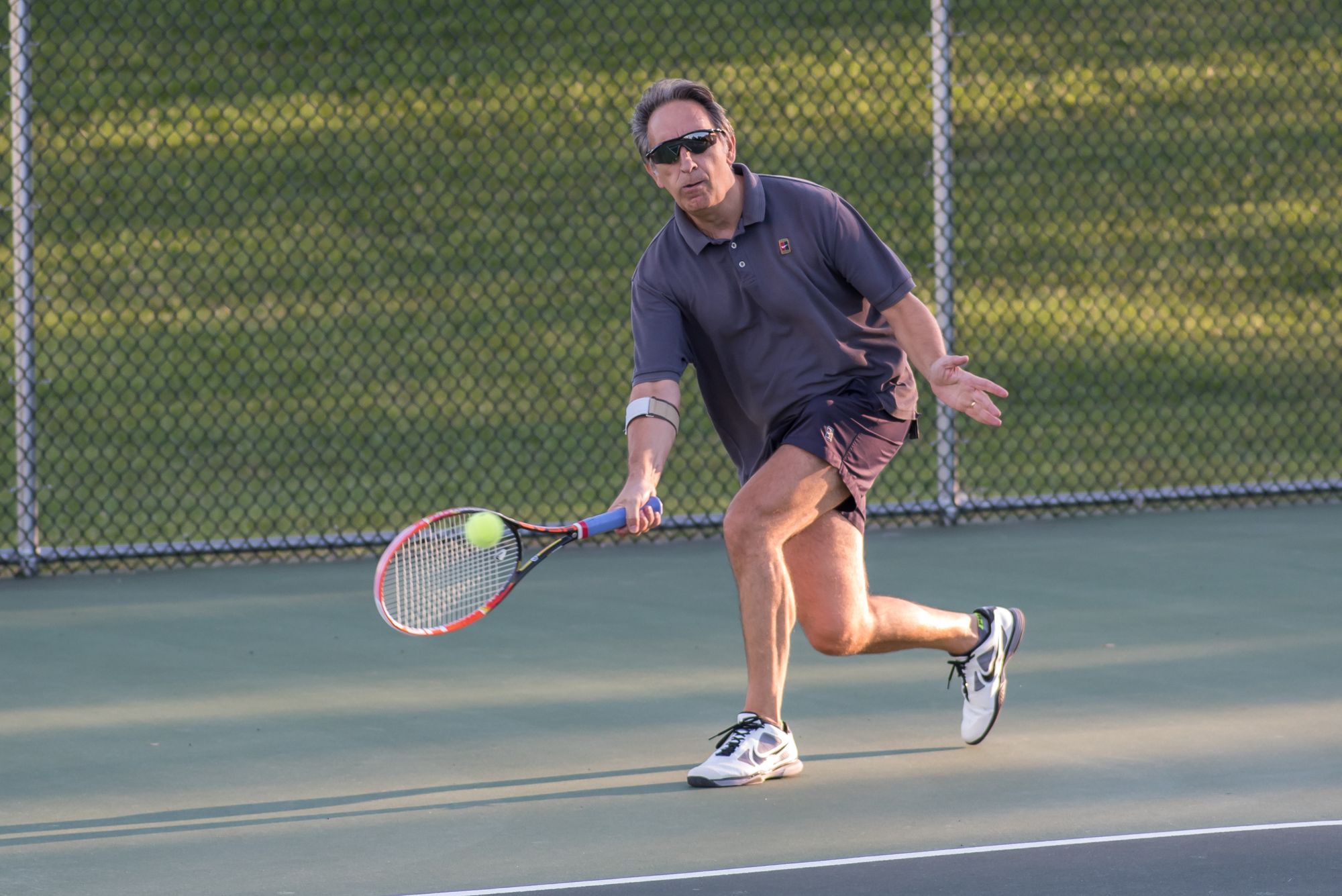 Mature adult tennis player reaching for a low ball during a controlled court movement.